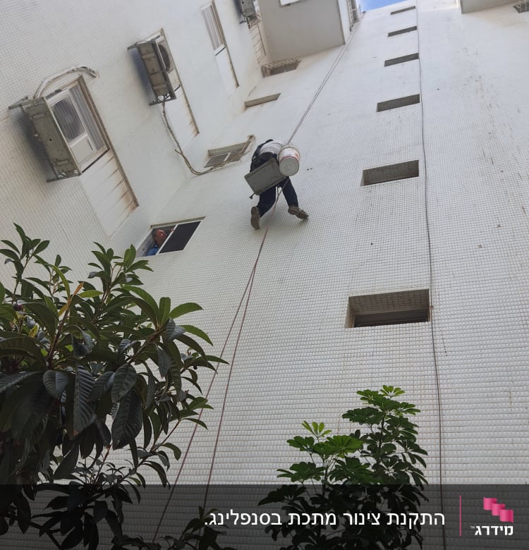 אדם תלוי על חבל עם דלי על קיר בניין